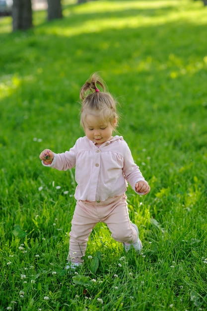 Het meisje in vrijetijdskleding maakt haar eerste stappen op het gras