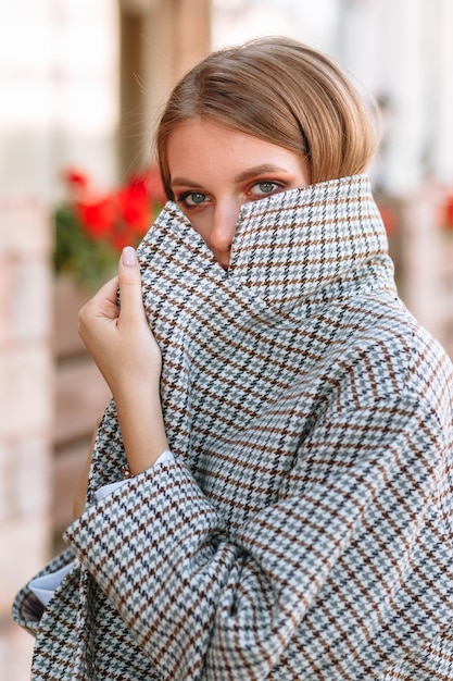 Het meisje is een model dat modieuze kleding op straat laat zien Achter het meisje staat een caféhek