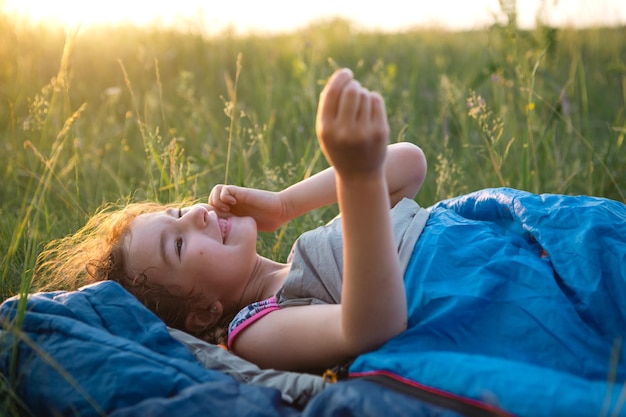 Het meisje is ontevreden over het krabben van muggenbeten kind slaapt in een slaapzak op het gras tijdens een kampeertrip Milieuvriendelijke openluchtrecreatie zomertijd Afstotend tegen slaapverstoring