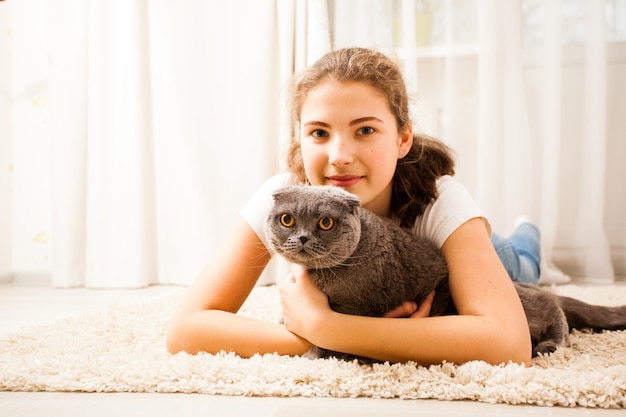 Het meisje knuffelt haar kat. ze liggen op het zachte tapijt in de kamer. de kat houdt zijn oren open