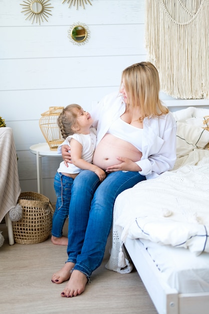 Foto het meisje koestert haar zwangere moeder die zich door het bed in de slaapkamer bevindt