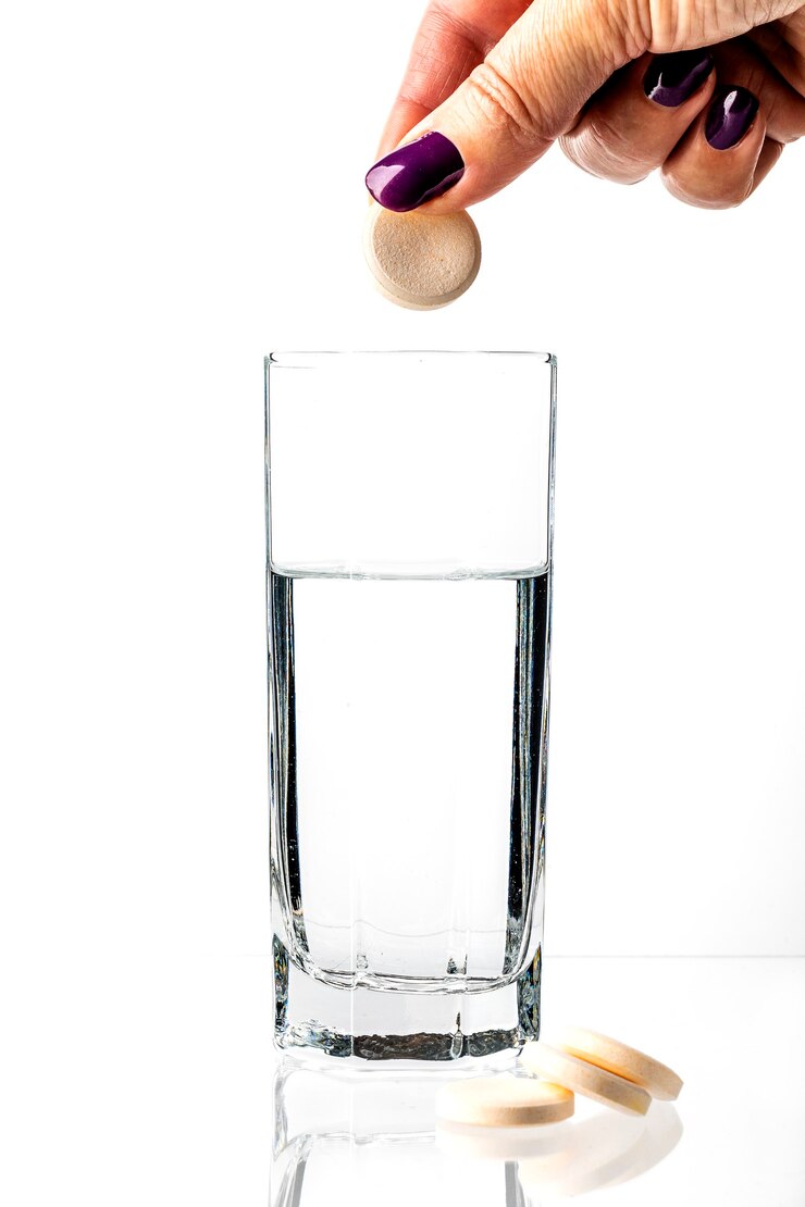 Het meisje laat een grote witte pil in een glas water vallen.