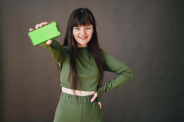 Het meisje lacht breed met uitgestoken hand waarin de telefoon met een groen scherm