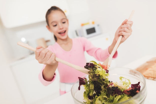 Het meisje leert een salade te bereiden in een lichte keuken