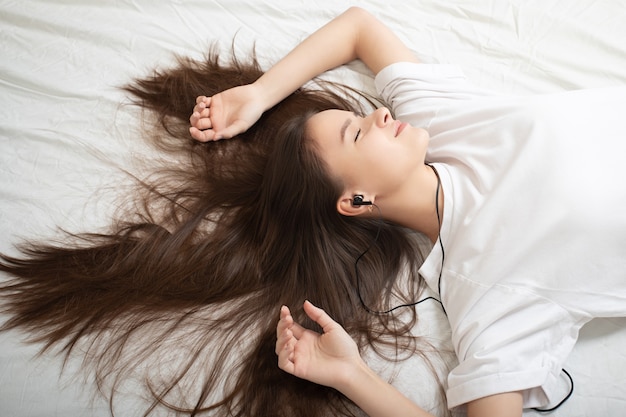 Het meisje ligt op het bed met een smartphone, luistert naar de radio met zijn ogen dicht.