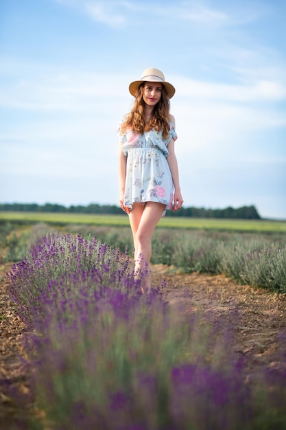 Het meisje loopt in de zomer met een hoed op een lavendelveld