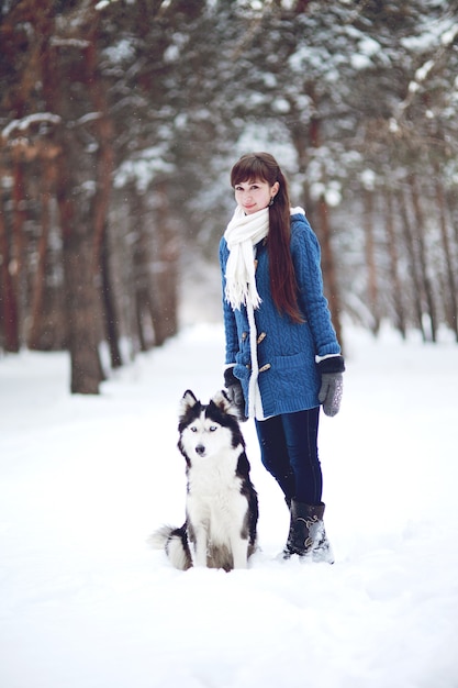 Het meisje loopt met de hond Siberische husky in een winters besneeuwd bos