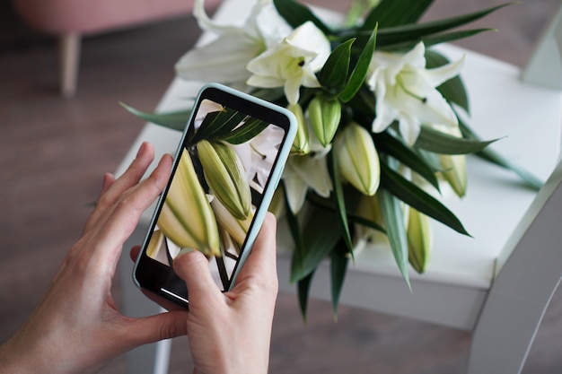 Het meisje maakt een foto op de telefoon. Fotografeert een boeket witte lelies. Opleiding mobiele fotografie. Geen zichtbare logo's.