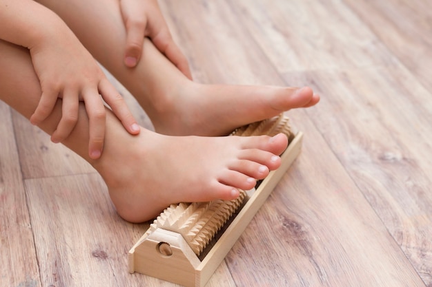 Het meisje masseert de voeten zelf op een speciale houten naaldmassager ter voorkoming van platvoeten, valgus. Ontspanning van de benen.