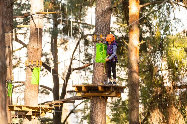 Het meisje met de oranje helm in het avonturenpark houdt de touwen vast