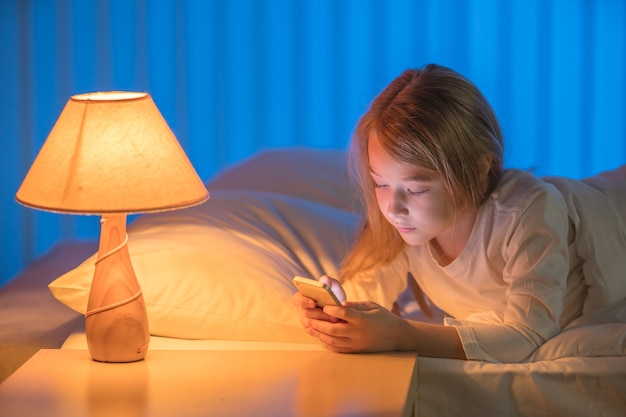 Het meisje met een telefoon lag op het bed. Avond nacht tijd