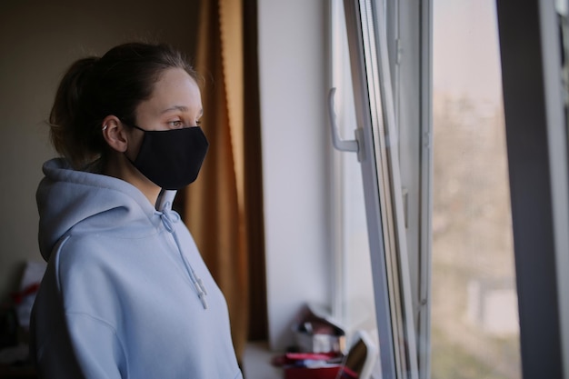 Het meisje met het zwarte masker staat geïsoleerd voor het raam van het huis