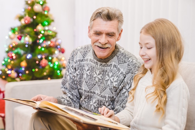 Het meisje met opa kijkt naar het fotoalbum bij de kerstboom