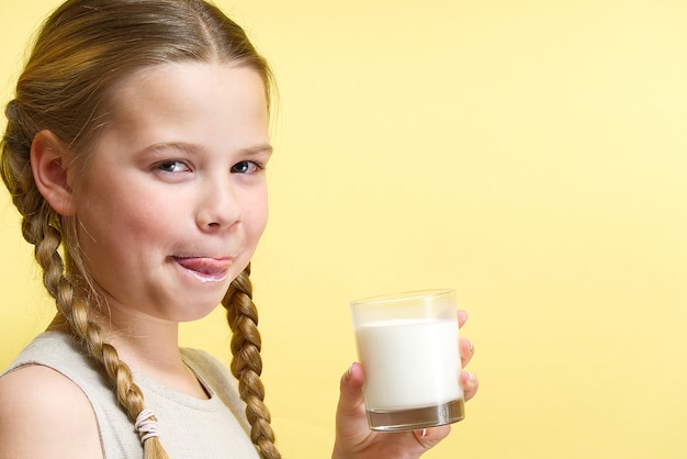 Het meisje met vlechten en een melksnor van consumptiemelk houdt glas melk terwijl status.