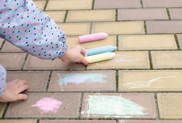 Het meisje neemt krijt om op de bestrating, stoep te schilderen. Straatkunst, onderwijs voor kinderen