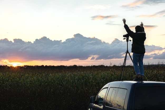 Foto het meisje op het dak van de auto fotografeert de zonsondergang met een statief.