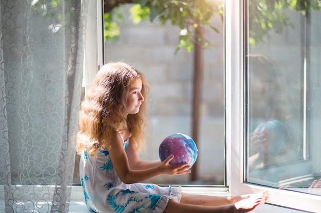 Het meisje op het raam van het huis houdt een lamp vast in de vorm van een planeet een wereldbol Vrede ecologie omgeving vredig