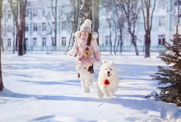 Het meisje rent met een Samojeed-puppy in een met sneeuw bedekt park op oudejaarsavond
