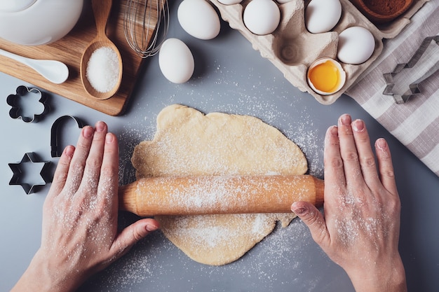 Het meisje rolt het deeg uit met een houten deegroller voor het maken van cupcakes of koekjes. Platte compositie met keukengerei en ingrediënten, kopieer ruimte. Concept van bakken voor de vakantie.