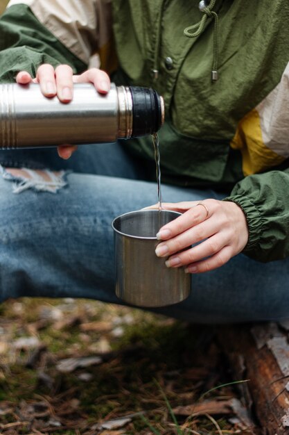 Het meisje schenkt aromatische thee uit een thermoskan in het bos. Picknick in het dennenbos