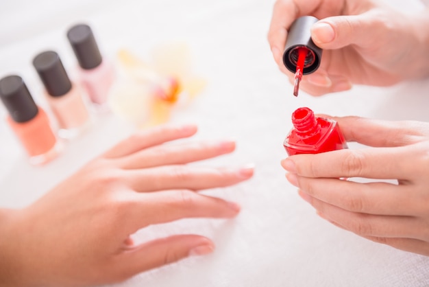 Het meisje schildert spijkers met rode vernis in de salon.