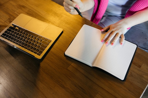 Het meisje schrijft in een notitieboekje het meisje zit en schrijft in een notitieboekje laptop in de buurt van vrouwelijke handen jong meisje doet notitieboekje en notitieboekje op een houten tafel zakelijk onderwijs freelance concept