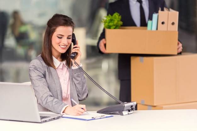 Het meisje spreekt telefonisch en werkt op de computer.