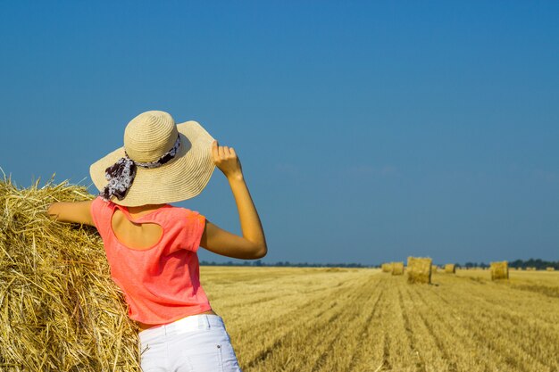 Het meisje staat in de buurt van een strobaal en kijkt in de verte in het veld