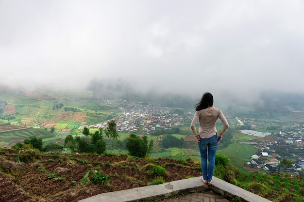 Het meisje staat tegen de achtergrond van een vallei in de wolken en mist