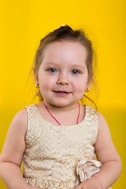 Foto het meisje stelt in mooie kleding op gele achtergrond