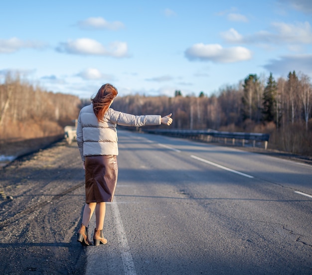 Foto het meisje stopt de auto op de snelweg met haar hand. stijlvolle vrouw op de weg stopt de auto op reis te gaan. een weg midden in het bos.