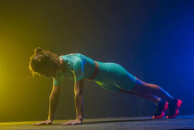 Het meisje traint op een donkere achtergrond moderne fitness op een geelblauwe achtergrond met een plek voor tekst