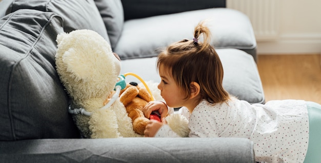 Het meisje van de babypeuter het spelen met van de arts uitrusting en pop speelgoed