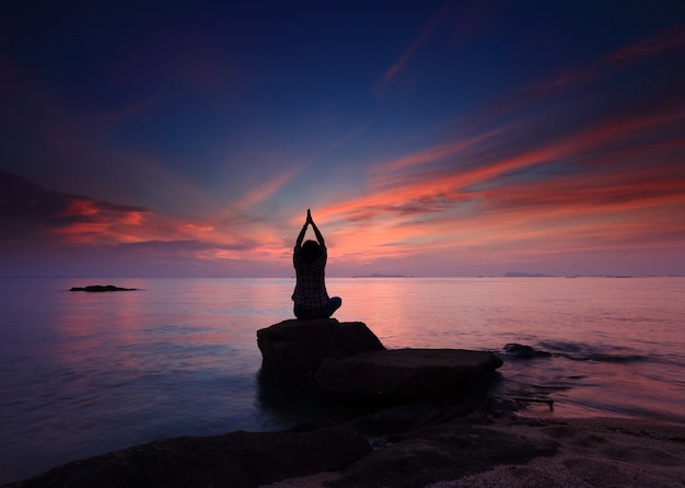 Het meisje van de silhouetyoga bij de strandzonsondergang