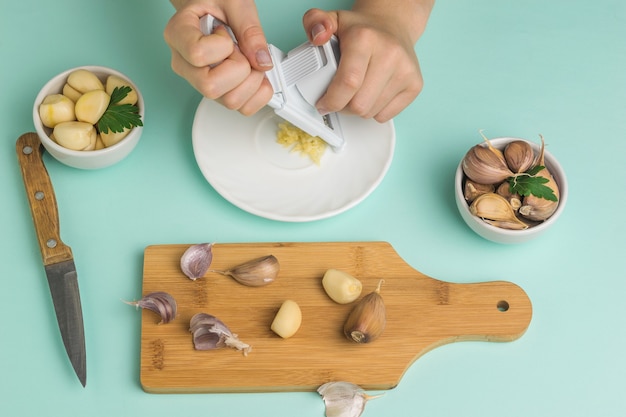 Het meisje verwerkt knoflook met een rasp op een snijplank. Een populaire specerij voor in de keuken.