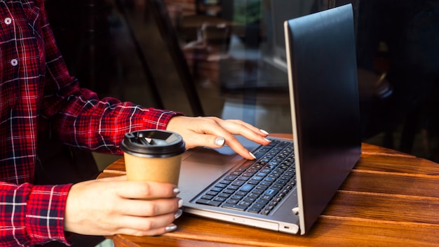 Het meisje werkt achter een laptop aan een tafel in een café naast een kop koffie