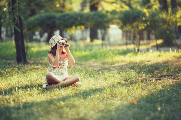 Het meisje wordt gespeeld door de zitting van de fotocamera op gras in park. Selfie doen en de wereld rondom fotograferen