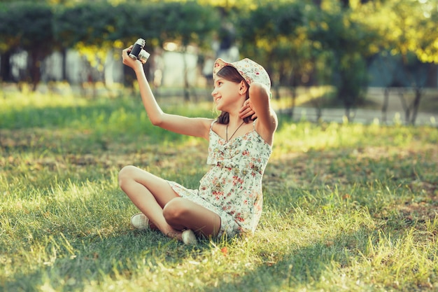 Het meisje wordt gespeeld door de zitting van de fotocamera op gras in park. Selfie doen en de wereld rondom fotograferen
