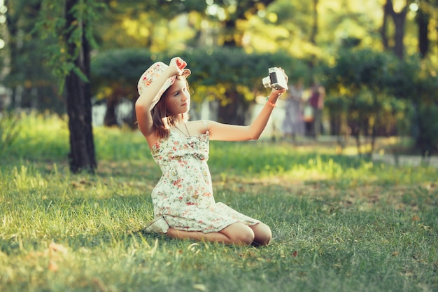 Het meisje wordt gespeeld door de zitting van de fotocamera op gras in park. Selfie doen en de wereld rondom fotograferen