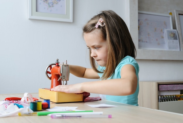 Het meisje zit aan de tafel en naait op een naaimachine.