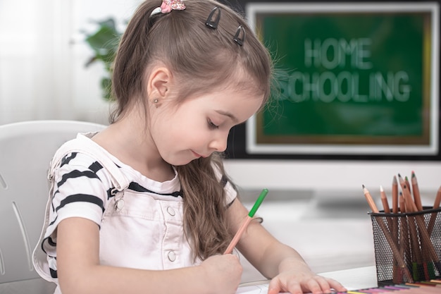 Het meisje zit aan tafel en maakt huiswerk. het kind leert thuis. thuisonderwijs en onderwijsconcept.