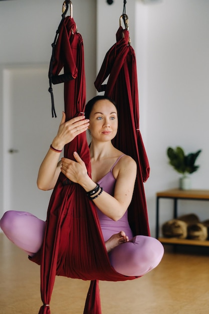 Het meisje zit in een hangende hangmat en doet yoga in de sportschool