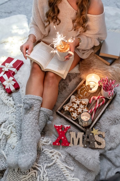 Het meisje zit in een kerstsfeer, drinkt een warm drankje en leest een boek.