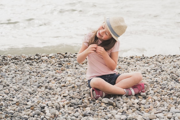 Het meisje zit op het strand kleine baby speelt met stenen bij de zee kinderen die zich graag laten verwennen