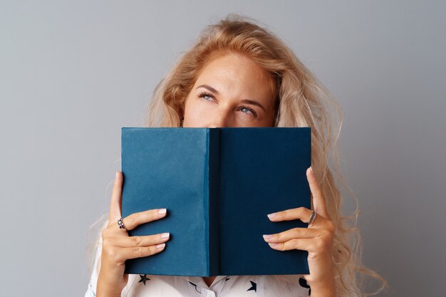 Het meisjestiener die van de student een boek in haar houdt overhandigt een grijze achtergrond