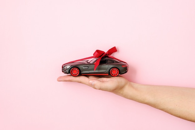 Het menselijke stuk speelgoed van de handholding automodel bond met een rood lint en een boog op roze achtergrond. autodealer en verhuur, auto als cadeau of cadeau, auto trekken, kans om een modern autoconcept te winnen