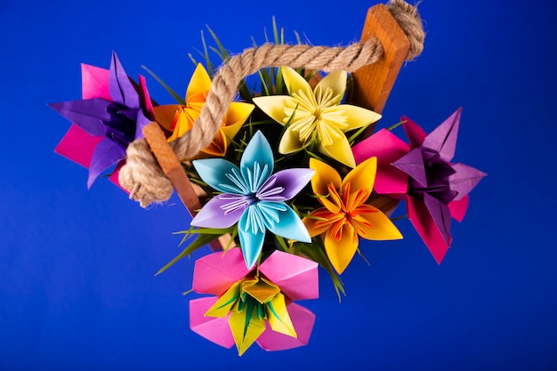 Het met de hand gemaakte gekleurde document bloemenboeket van het origamiboeket ambachtkunst in een mand met gras in de studio op gekleurde achtergrond topshot