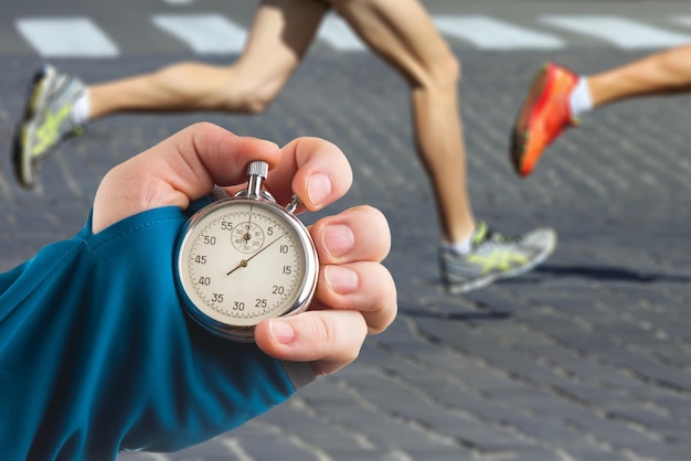 Foto het meten van de loopsnelheid van een atleet met behulp van een mechanische stopwatchhand met een stopwatch op de achtergrond van de benen van een hardloper