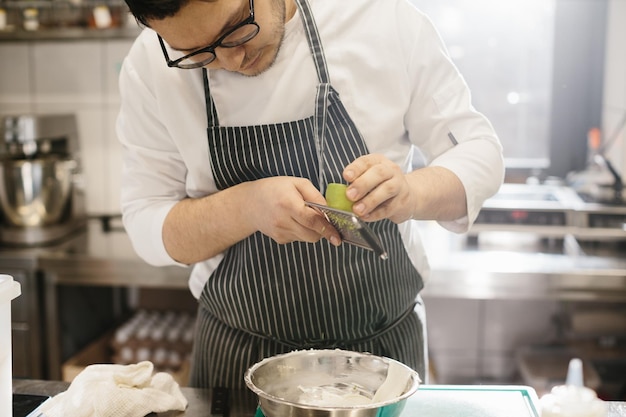 Het middelste gedeelte is een portret van een chef-kok die limoenschil raspt Het concept van koken in een restaurant