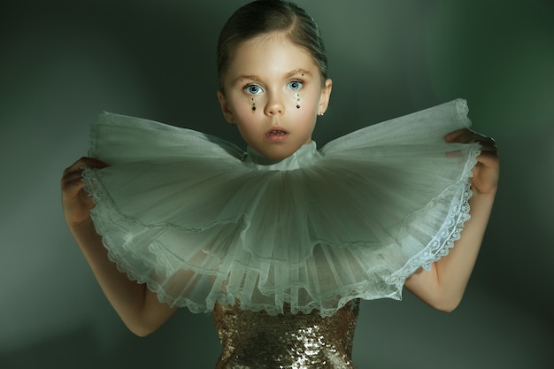 Het mode-portret van een jong mooi tienermeisje in een gouden jurk in de studio. De beauty, fashion, glow, make-up en stralende concepten. Kaukasisch model